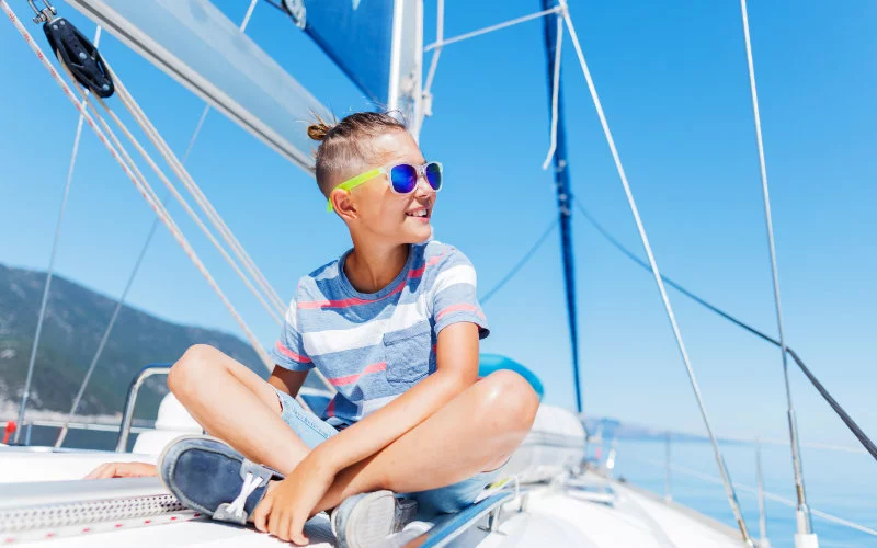 Zdjęcie chłopiec siedzi na pokładzie jachtu w okularach przeciwsłonecznych